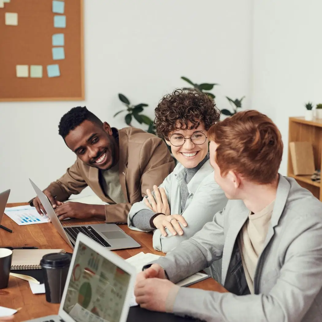 Employees sitting by a desk with laptops working and laughing